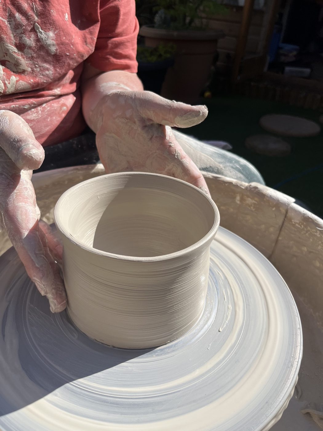 Hands shaping a pot on the wheel in the sunshine